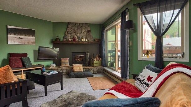A cozy living room with a stone fireplace, a television, and a comfortable couch. - Apex Mountain ~ Beaconsfield Getaway (Apex Mountain Resort)