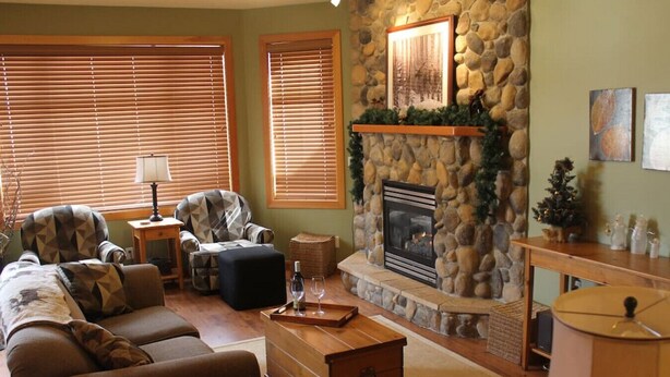 A cozy living room with a stone fireplace, comfortable seating, and a small table with a bottle and glasses. - Apex Mountain ~ Moose Lodge (Apex Mountain Resort)