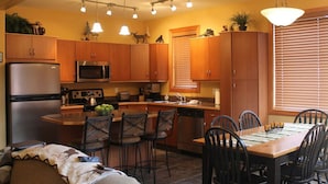 A modern kitchen with wooden cabinets, a stainless steel refrigerator, and a central island with bar stools. - Apex Mountain ~ Moose Lodge (Apex Mountain Resort)
