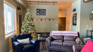 Una sala de estar acogedora con un árbol de Navidad, sofás de cuero y un letrero que indica 'SKI LODGE'.