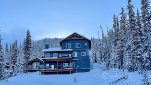 Una cabaña de dos pisos con balcón y terraza, rodeada de árboles cubiertos de nieve.