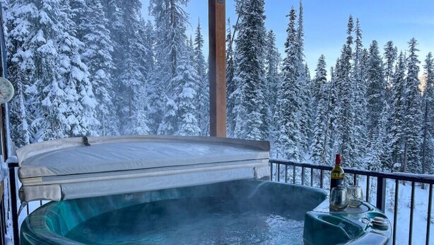 Un jacuzzi en un balcón con vista a un bosque nevado.