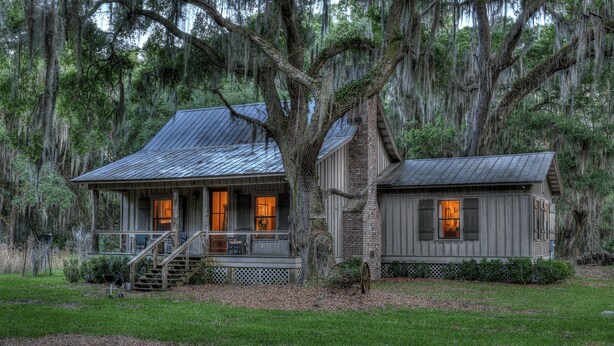 A rustic cabin with a porch, a chimney, and a small attached structure. - 3BR Chachalaca Retreat on Sapelo w/ firepit, screened-in porch, & beach supplies (Sapelo Island)