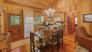 A wooden interior with a dining table, chairs, a refrigerator, a microwave, and a chandelier. - 3BR Chachalaca Retreat on Sapelo w/ firepit, screened-in porch, & beach supplies (Sapelo Island)