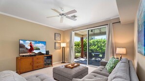 Ein Wohnzimmer mit Fernseher, Deckenventilator und einer Schiebetür zu einer Terrasse.