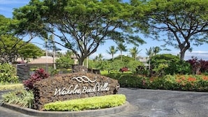 Schild für die Waikoloa Beach Villas mit einem angelegten Garten und Bäumen.