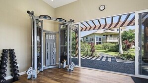 Ein Fitnessstudio mit Trainingsgeräten, einer Hantelbank und Blick auf ein Haus durch große Schiebetüren.