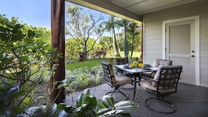 Eine überdachte Terrasse mit Tisch und Stühlen, umgeben von üppiger Vegetation und Palmen.