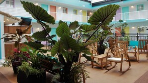 Un espacio interior amplio con plantas en macetas grandes, mecedoras de madera y un balcón con barandillas de colores.