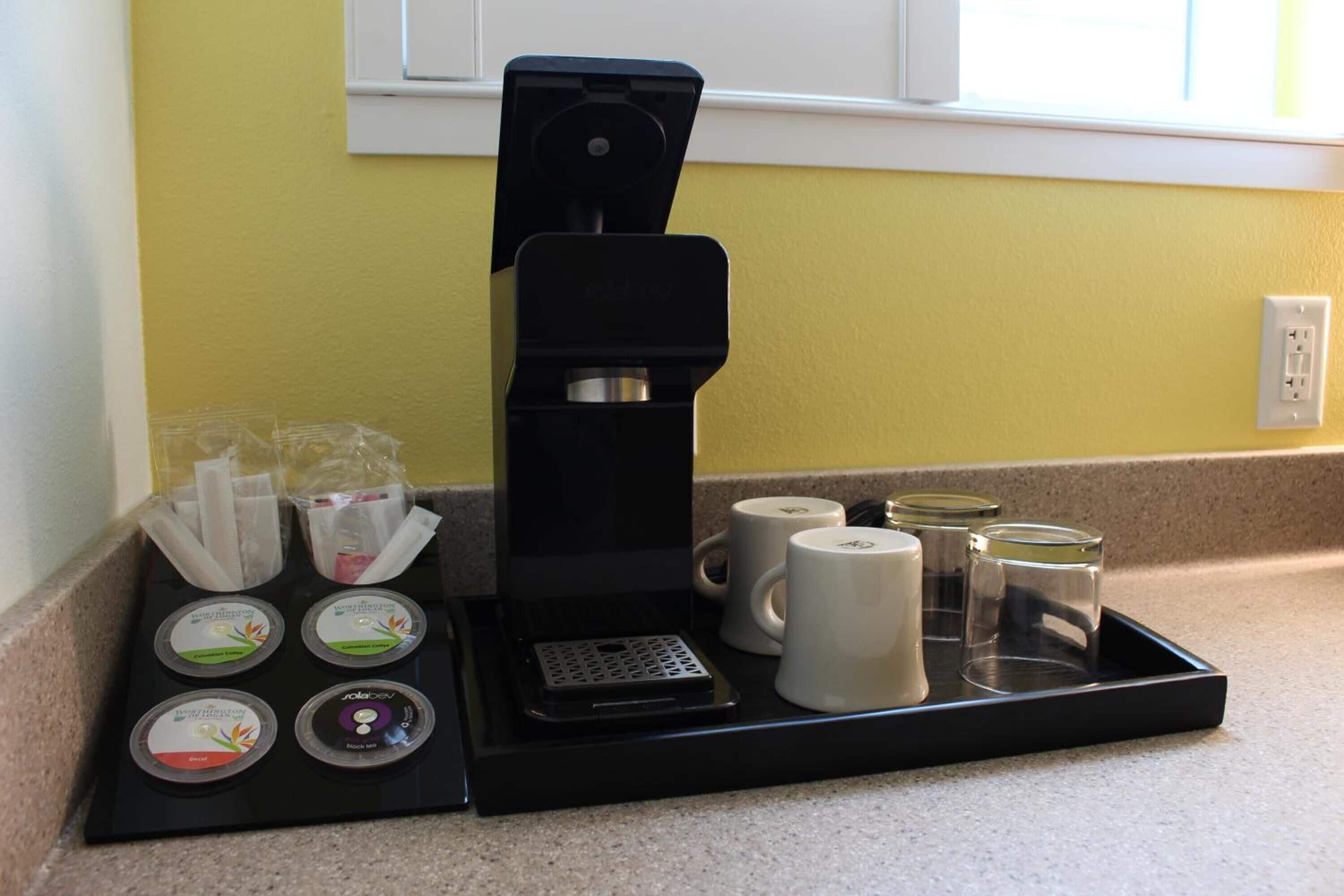 Angolo caffè con macchina da caffè, tazze monouso e vassoio con cialde.
