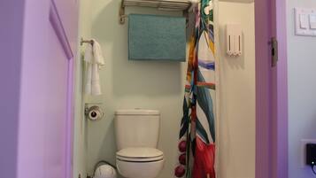 A bathroom with a toilet, a towel rack, a shower curtain, and a wall-mounted light switch.