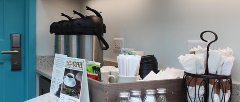 A coffee station with a coffee machine, mugs, salt and pepper shakers, and a menu sign.