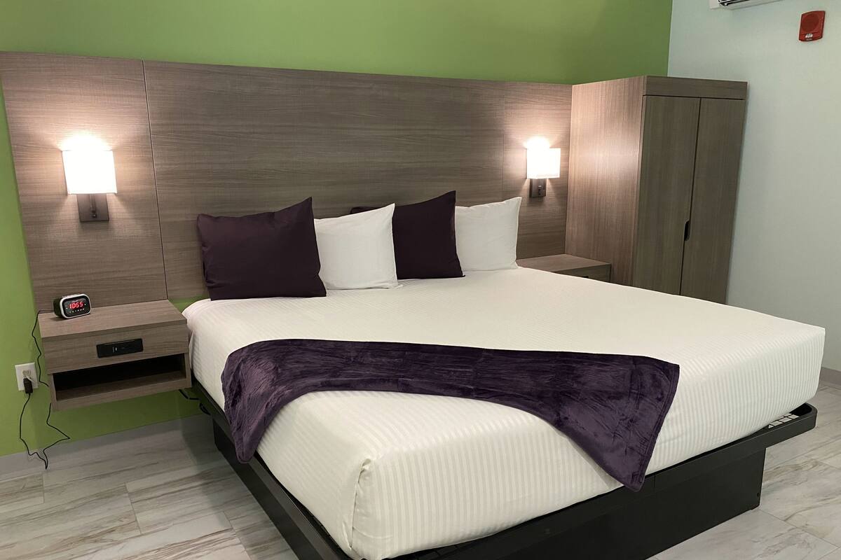 A modern bedroom with a large bed, two bedside tables, a nightstand, a wardrobe, and wall-mounted lights.