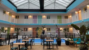 Un espacio interior de varios niveles con techo de vidrio, una piscina y diferentes zonas de estar.