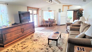 Ein Wohnzimmer mit einem Holzkabinett, einem Fernseher, einem floralen Teppich, einer Couch und einem Essbereich mit Tisch und Stühlen.