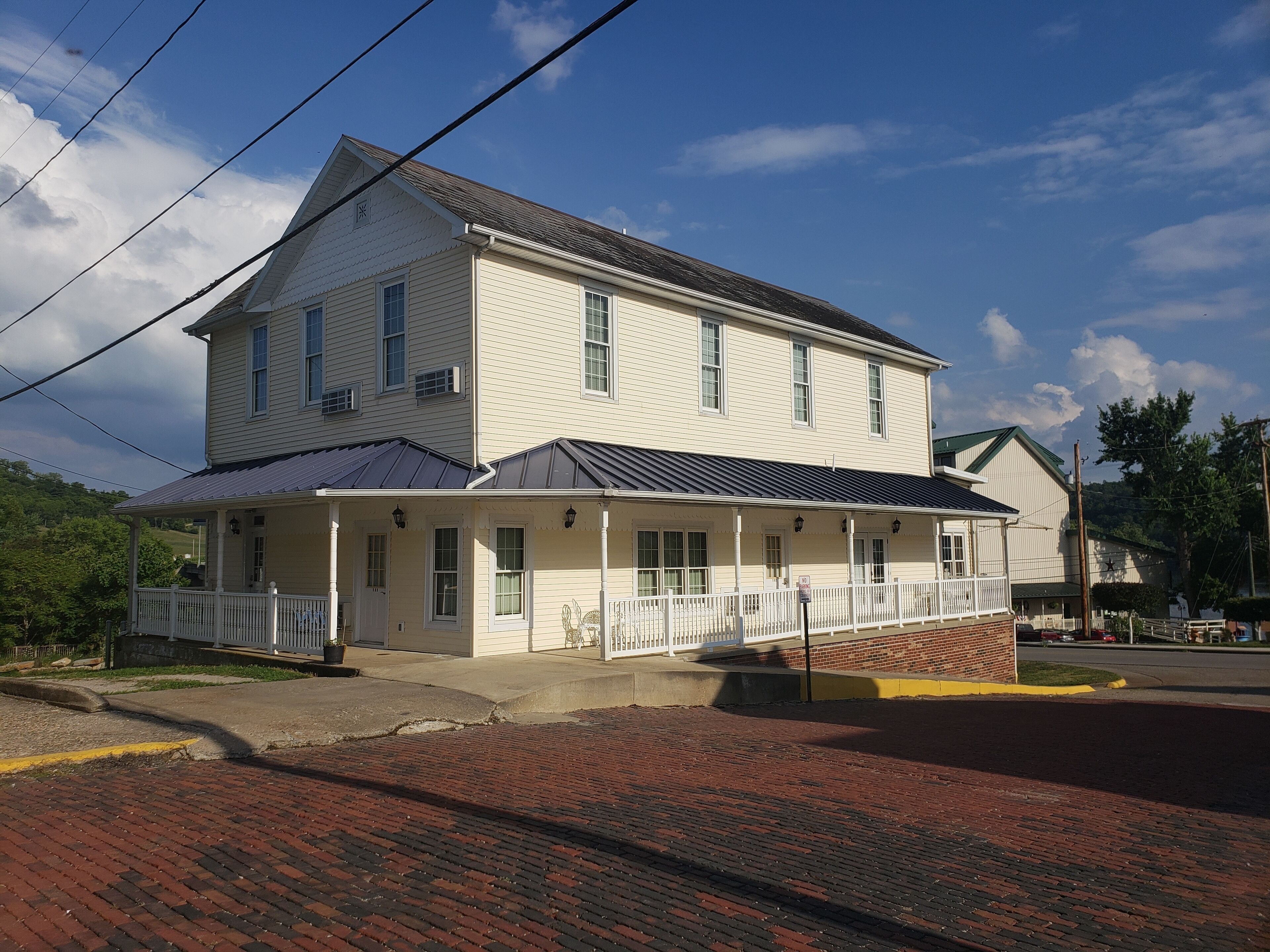 A two-story building with a porch, a brick driveway, and a street in the background.