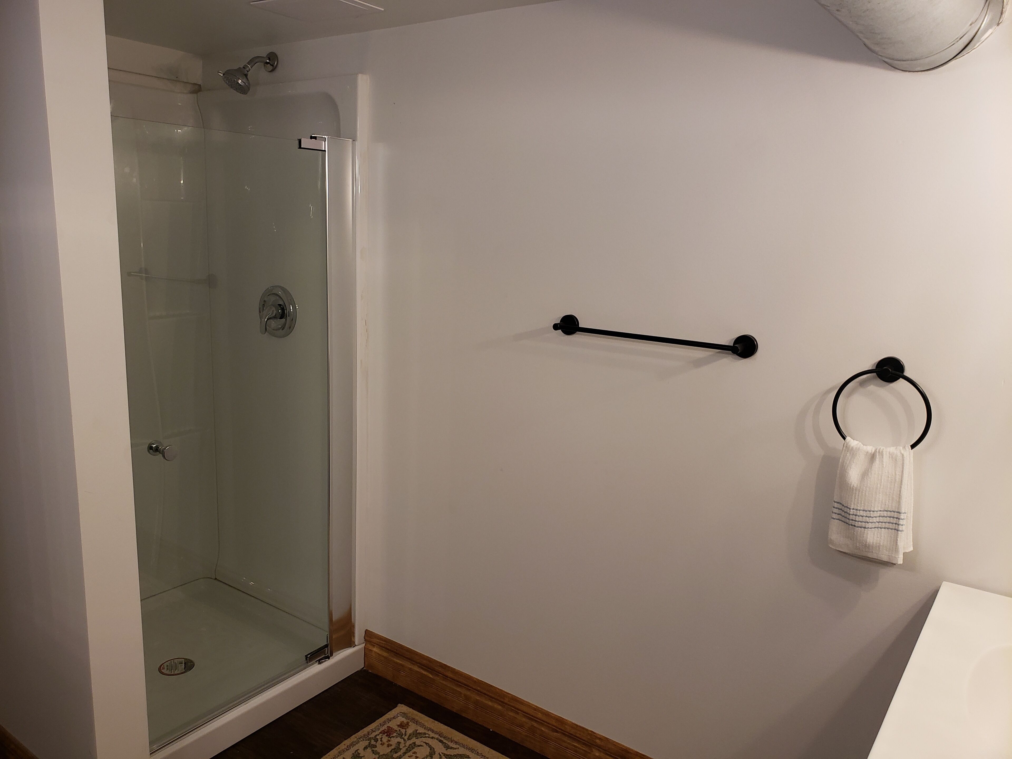 A bathroom with a glass shower enclosure, a towel rack with a towel, and a wooden floor.