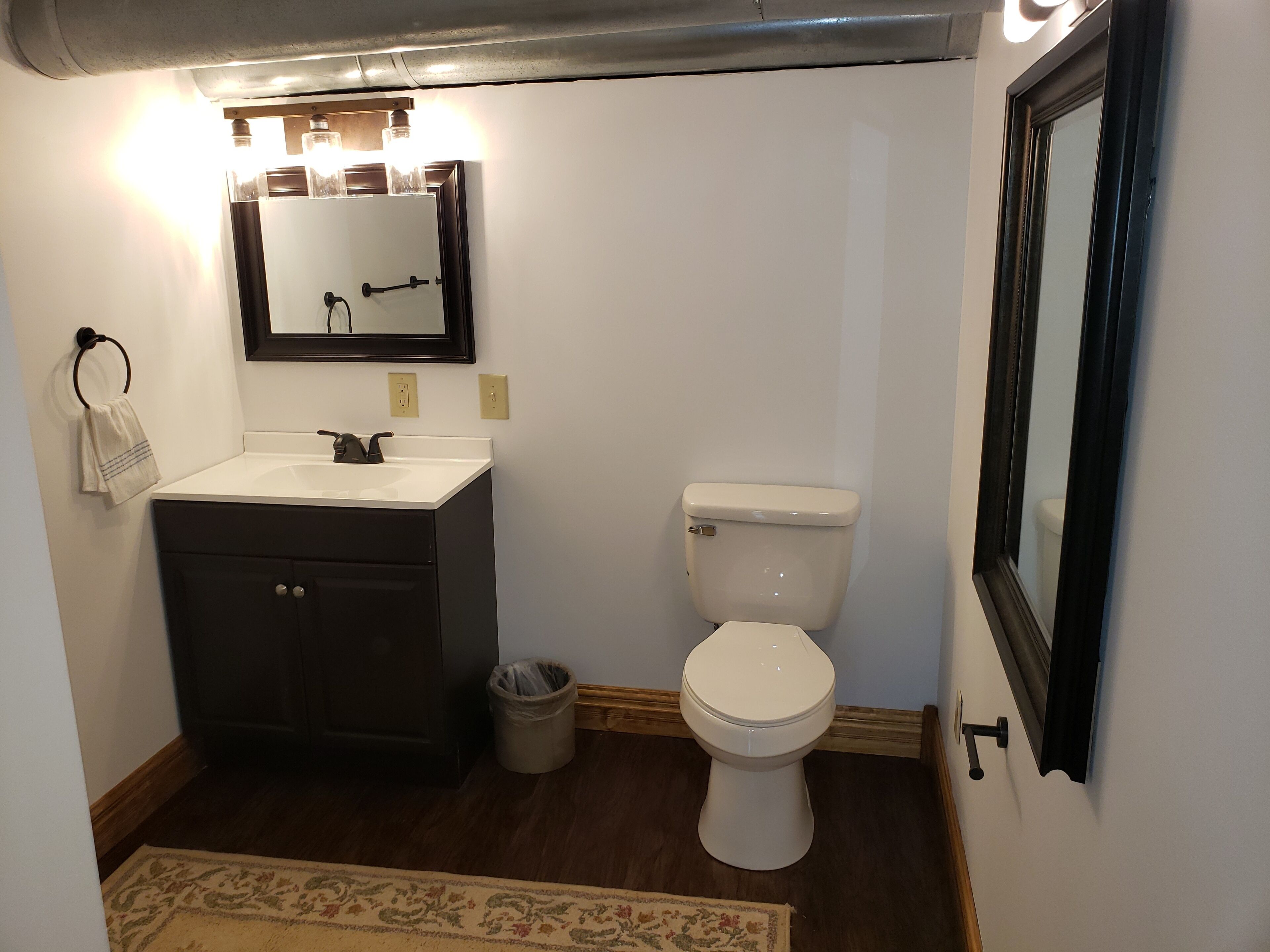 Een badkamer met een wastafel, spiegel, toilet en een prullenbak.