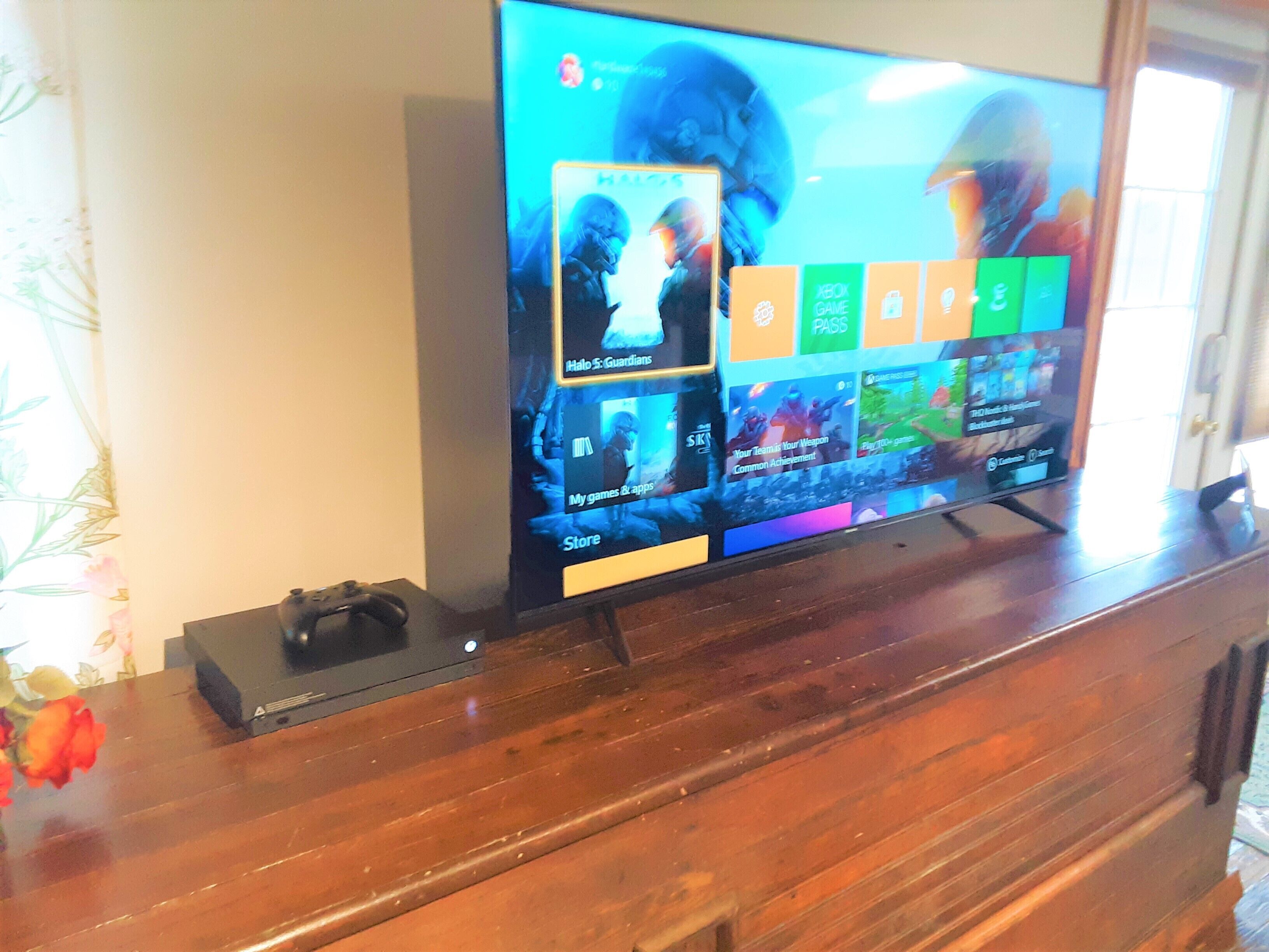 A television on a wooden stand displaying a video game interface with various game icons and a game controller beside it.