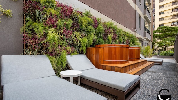 A modern outdoor seating area with lounge chairs and a small table, surrounded by a lush vertical garden. -  Charlie Vila Nova Conceição Jacques Félix (São Paulo)