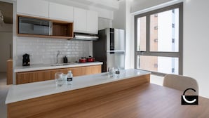 A modern kitchen with white cabinets, a stainless steel refrigerator, and a large window providing a view of the city. -  Charlie Vila Nova Conceição Jacques Félix (São Paulo)
