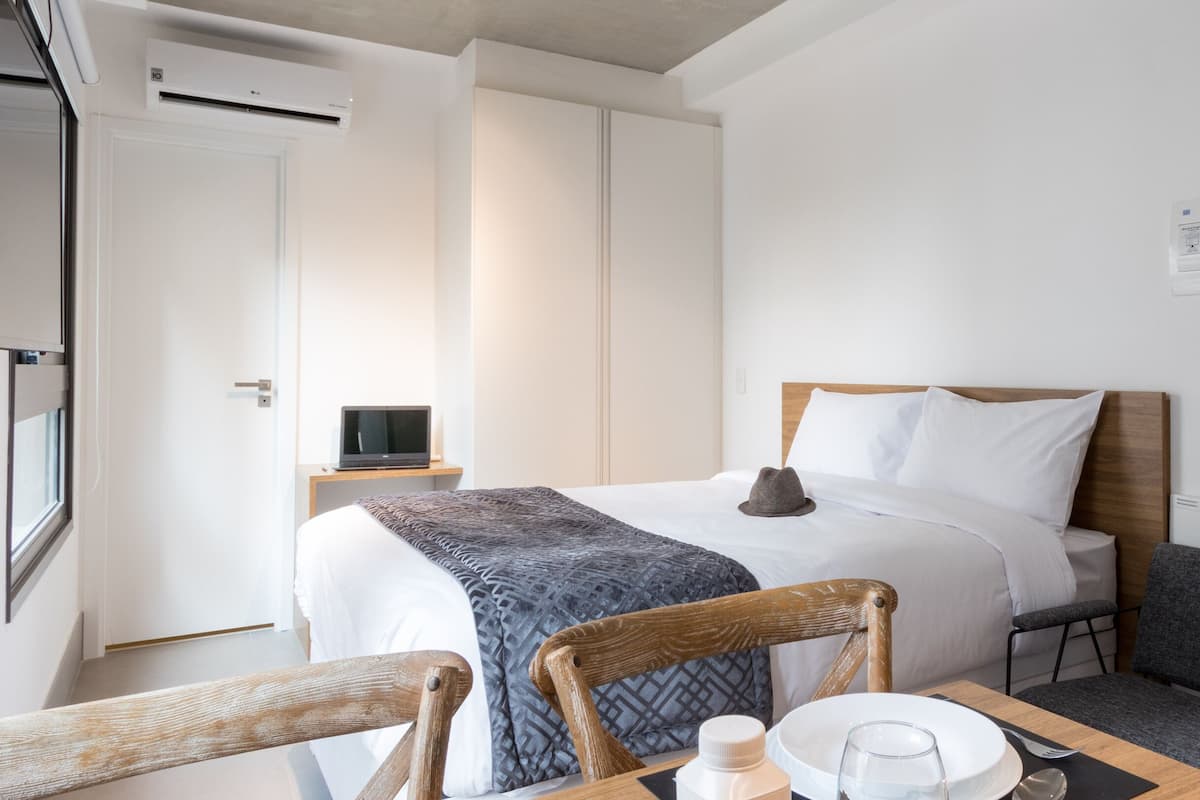Een hotelkamer met een bed, nachtkastje, stoel en een klein tafeltje met een glas en fles.
