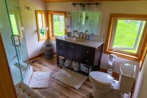A bathroom with a glass shower, wooden flooring, a sink with a mirror above, and a toilet.