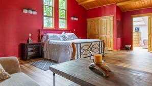 A bedroom with a wooden ceiling, a bed with a white bedspread, a nightstand, and a window with a view of trees.