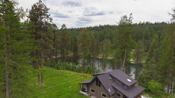 A two-story cabin with a large deck, surrounded by a forest and a lake.