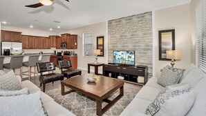 A modern living room with a sofa, coffee table, and a TV. There is a kitchen area with cabinets and appliances. - Modern Home, Big Pool Area Near Disney, CDC Cleaning 4cg456 (Davenport)