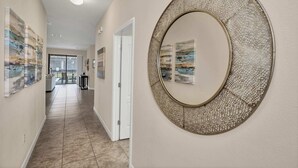 A hallway with a large circular mirror, artwork on the walls, and a door leading to a room with a view. - Modern Home, Big Pool Area Near Disney, CDC Cleaning 4cg456 (Davenport)