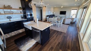 A modern kitchen with a central island, dark cabinetry, and a dining area with a large window. - Emma's View On Lay Lake<br>SUMMERTIME ON LAY LAKE IS THE BEST!!☀️ (Shelby)