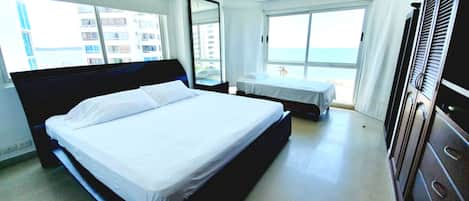 A hotel room with a large bed, a smaller bed, a desk, and a view of the beach.