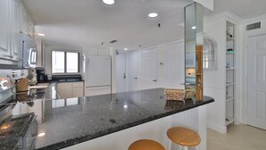 Eine Küche mit schwarzer Granitabdeckung, weißen Schränken und einem großen Spiegel. Zwei Holzbarhocker stehen an der Arbeitsfläche.