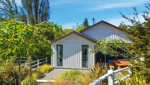 Une maison moderne avec une façade blanche, une terrasse en bois et un jardin qui l’entoure.