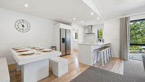 Une cuisine moderne avec un îlot central, un coin repas agrémenté d’une horloge, et une vue sur l’extérieur.