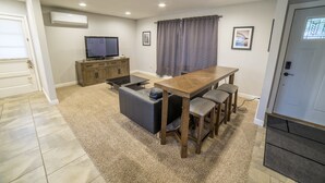 A modern living room with a wooden dining table, a black sofa, and a television.