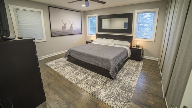 A bedroom with a bed, a ceiling fan, a large mirror, and a window with blinds.