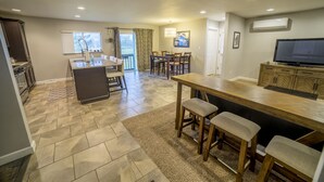 A modern kitchen with a dining area, a TV, and a large window.