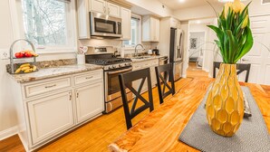 A modern kitchen with white cabinets, stainless steel appliances, and a wooden dining table. - The Inn at Newton Highlands, boutique apartment-hotel (Newton)