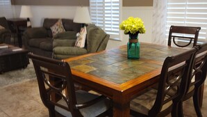 Un comedor con una mesa y sillas de madera, un jarrón de flores amarillas y una ventana con persianas.