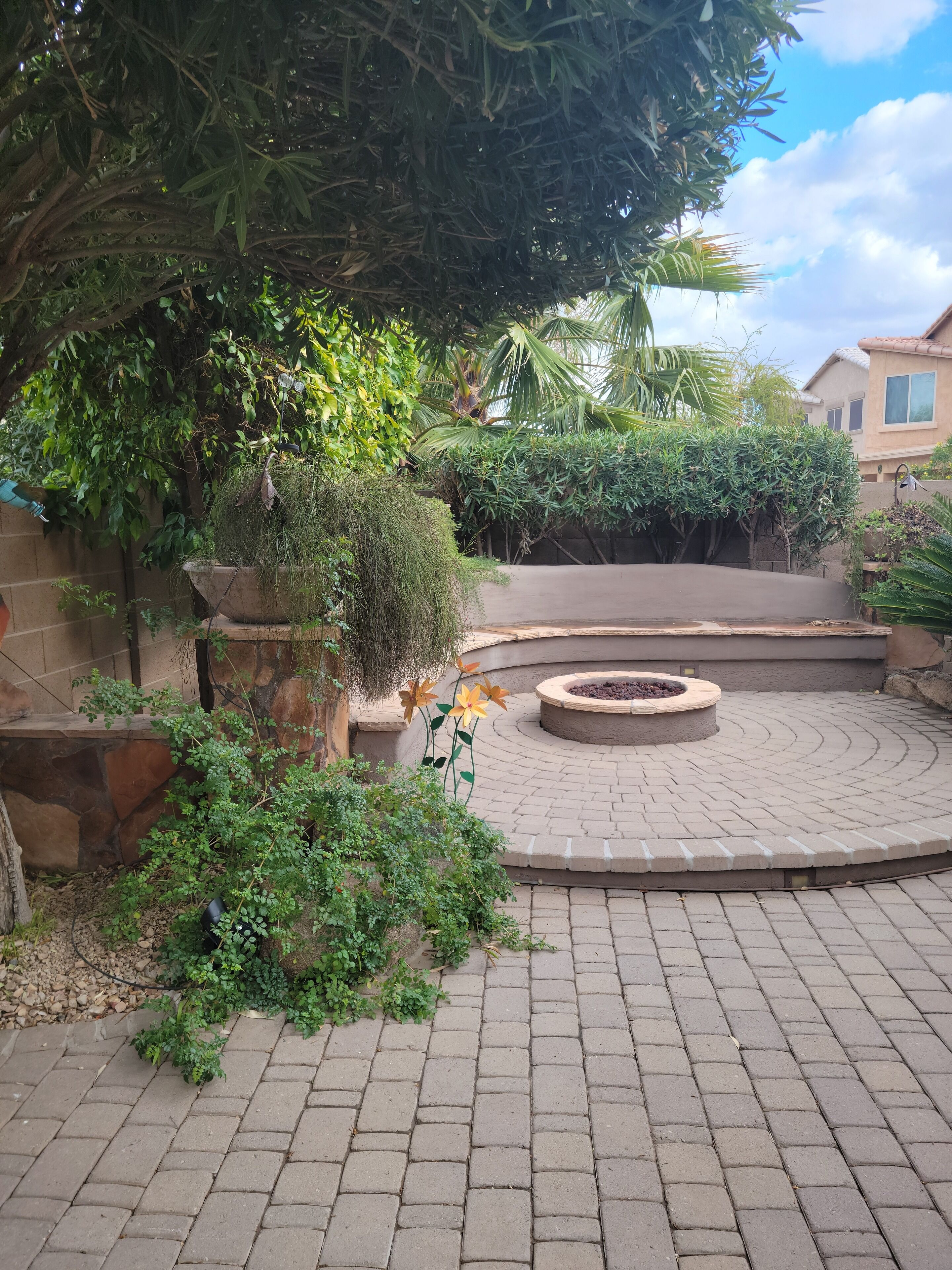 Un patio empedrado con un espacio de estar circular, rodeado de diversas plantas y árboles.