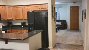 Una cocina con armarios de madera, un refrigerador negro y un pequeño cubo de basura.