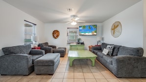 Ein Wohnzimmer mit grauen Sofas, einem grünen Couchtisch und einem Fernseher an der Wand.
