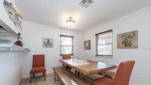 Ein Essbereich mit Holztisch, Bänken und Stühlen. An den Wänden befinden sich Kunstwerke, und eine Leuchte hängt von der Decke.