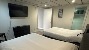 Ein Hotelzimmer mit zwei Betten, einem an der Wand befestigten Fernseher, einem Schminktisch und einem Kleiderschrank mit Kleidung.