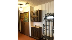Un couloir avec une porte en bois, un tableau d’affichage, un meuble et un banc en métal.