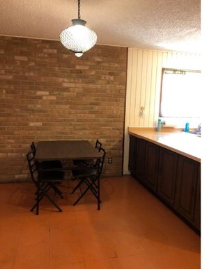 A kitchen with a brick wall, a dining table with chairs, and a hanging light fixture.