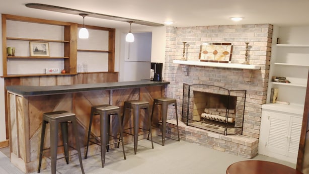 A bar area with a brick fireplace, wooden shelves, and bar stools. - Hot Tub and Private Pool, 7 Bedroom, 4 Bathroom Home. Sleeps 16 comfortably. (Warrenton)