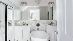 A bathroom with a freestanding bathtub, two sinks, and a large mirror above the vanity. - The Belle at Avery Lafayette Suite (Morganton)